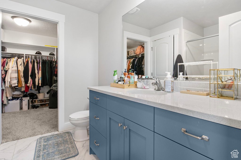 Full bath with vanity, a spacious closet, toilet, a shower stall, and marble look tile flooring
