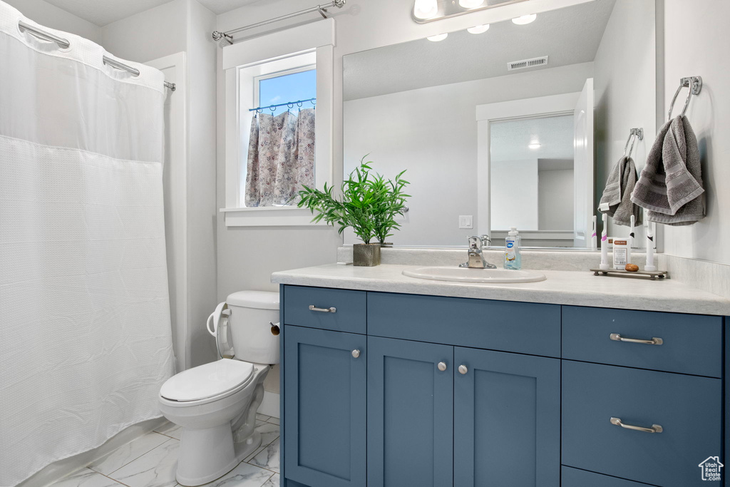Bathroom with toilet, vanity, marble look tile flooring, and curtained shower