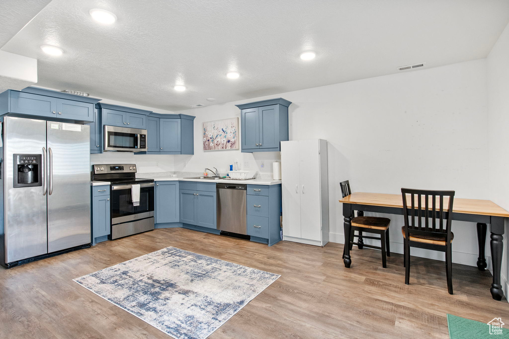 Kitchen featuring stainless steel appliances, a sink, light wood-type flooring, light countertops, and blue cabinetry