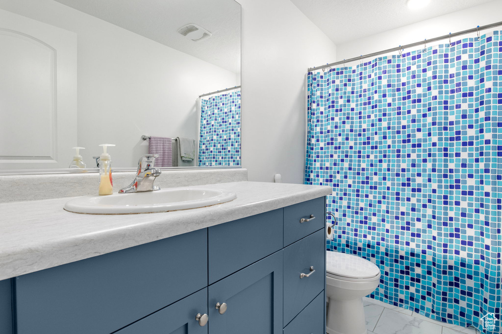 Bathroom featuring vanity, toilet, marble look tile flooring, and curtained shower