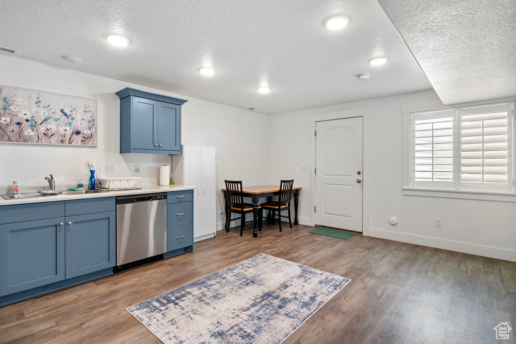 Kitchen featuring dishwasher, a textured ceiling, blue cabinetry, wood finished floors, and a sink
