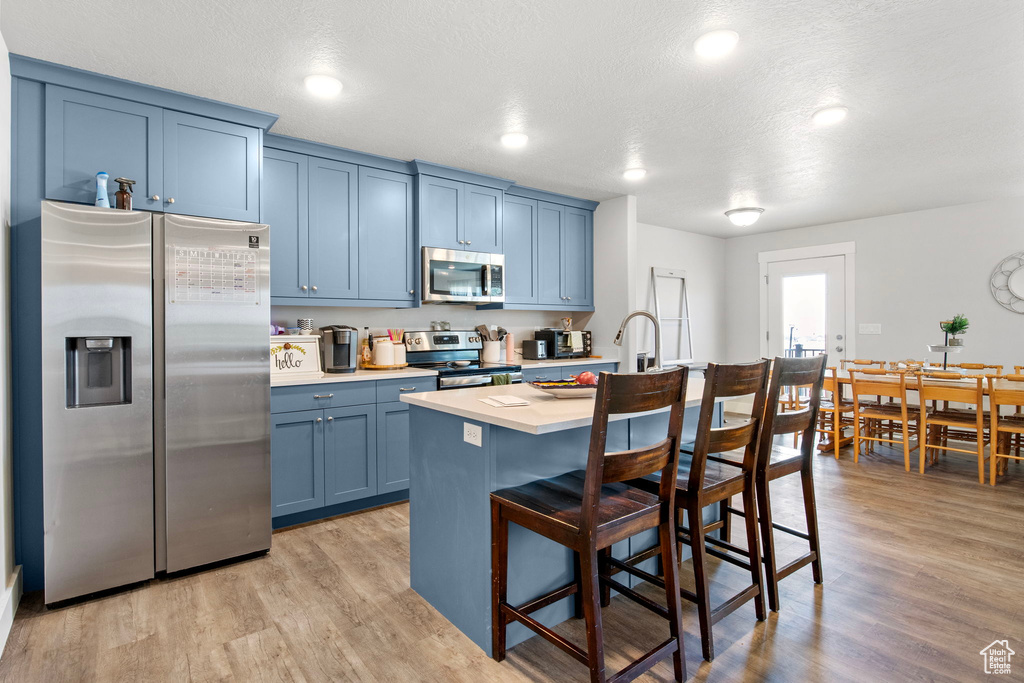 Kitchen featuring appliances with stainless steel finishes, blue cabinetry, light countertops, a kitchen breakfast bar, and an island with sink