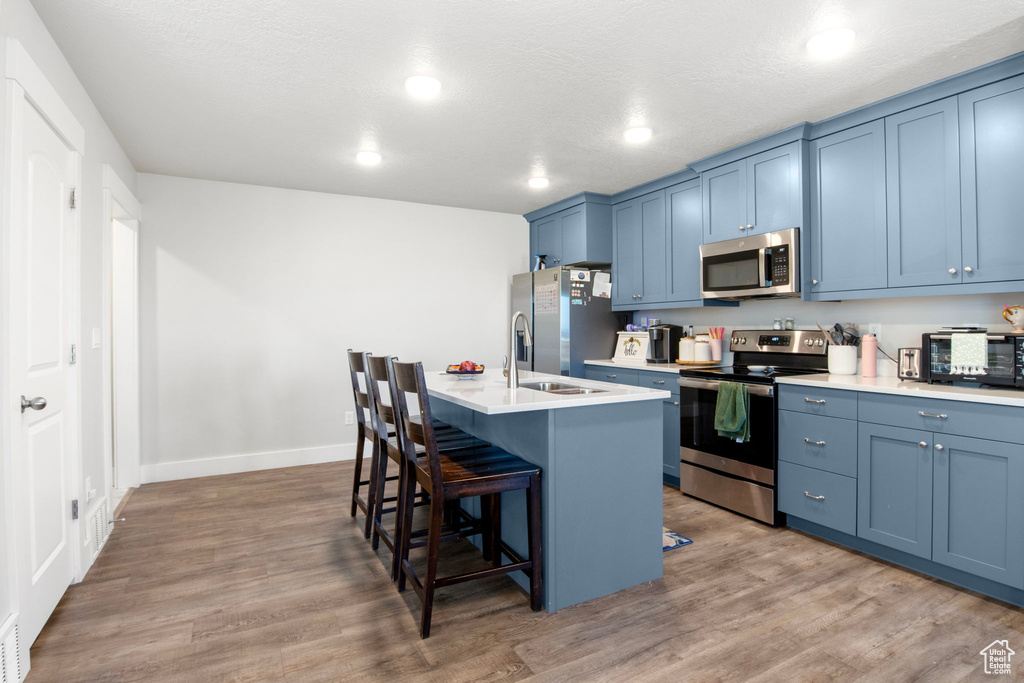 Kitchen with appliances with stainless steel finishes, blue cabinets, a breakfast bar, an island with sink, and recessed lighting