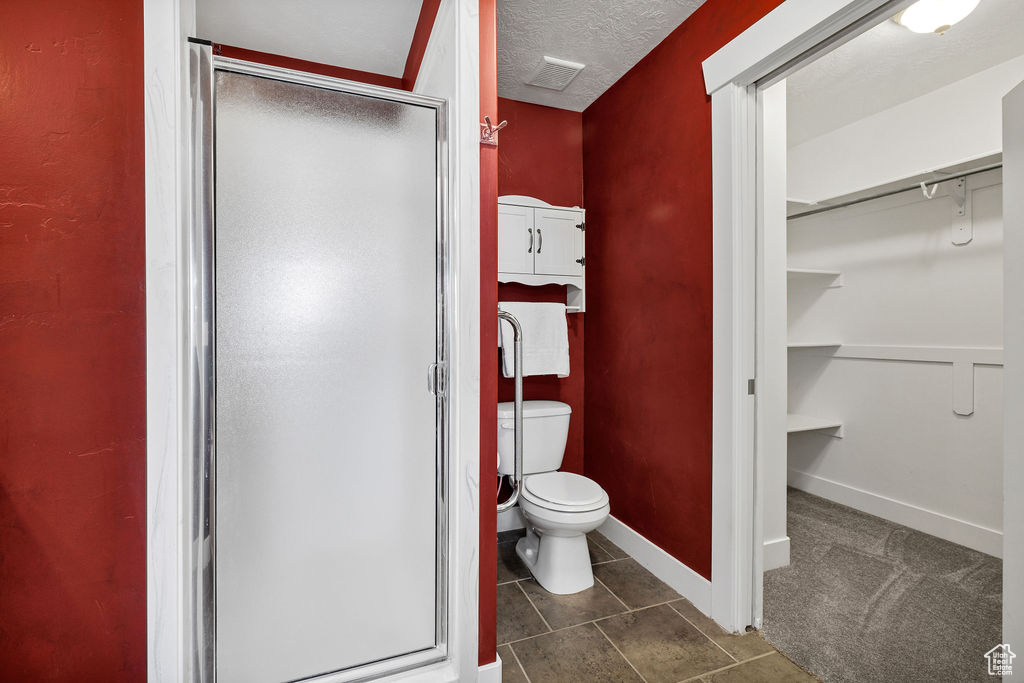 Full bath with a stall shower, a spacious closet, toilet, tile patterned floors, and a textured ceiling