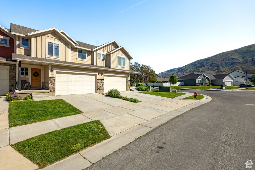 Multi unit property featuring a mountain view, an attached garage, driveway, stone siding, and board and batten siding