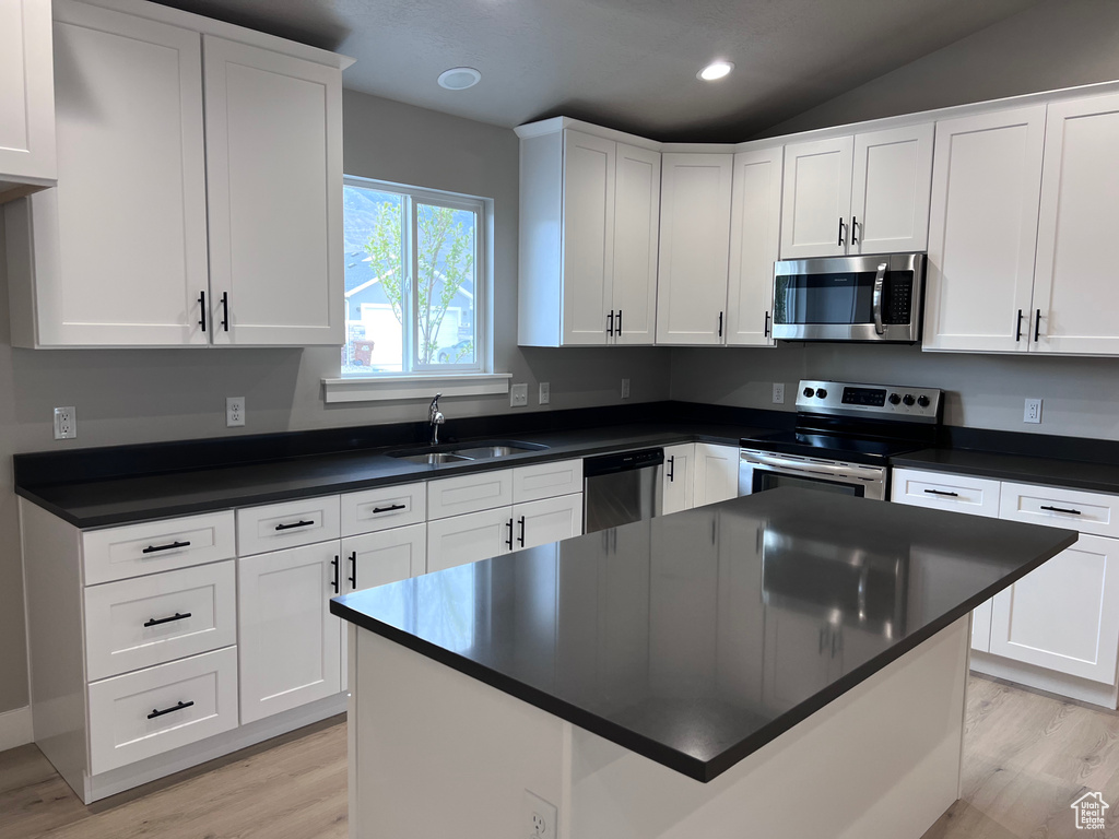 Kitchen featuring appliances with stainless steel finishes, a sink, light wood-type flooring, dark countertops, and white cabinetry