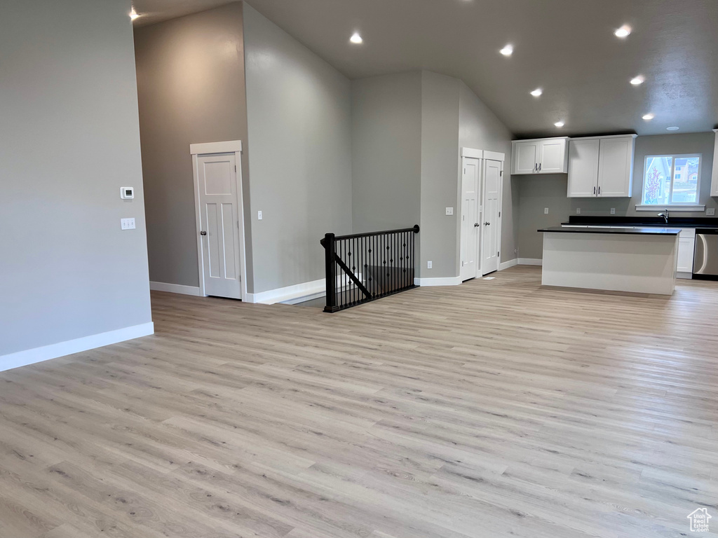 Kitchen with dark countertops, lofted ceiling, white cabinets, stainless steel dishwasher, and open floor plan