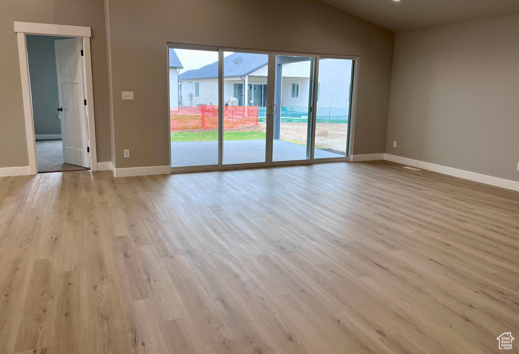 Unfurnished room featuring wood finished floors, lofted ceiling, and baseboards