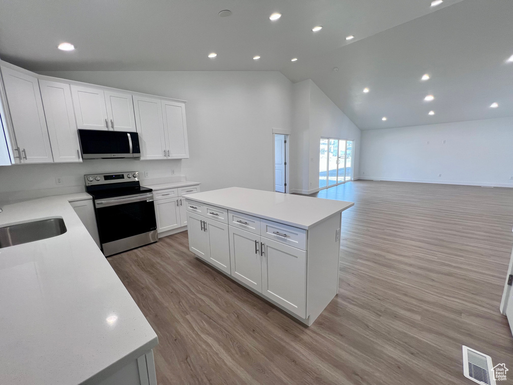 Kitchen with stainless steel electric range, a center island, light countertops, a sink, and white cabinetry