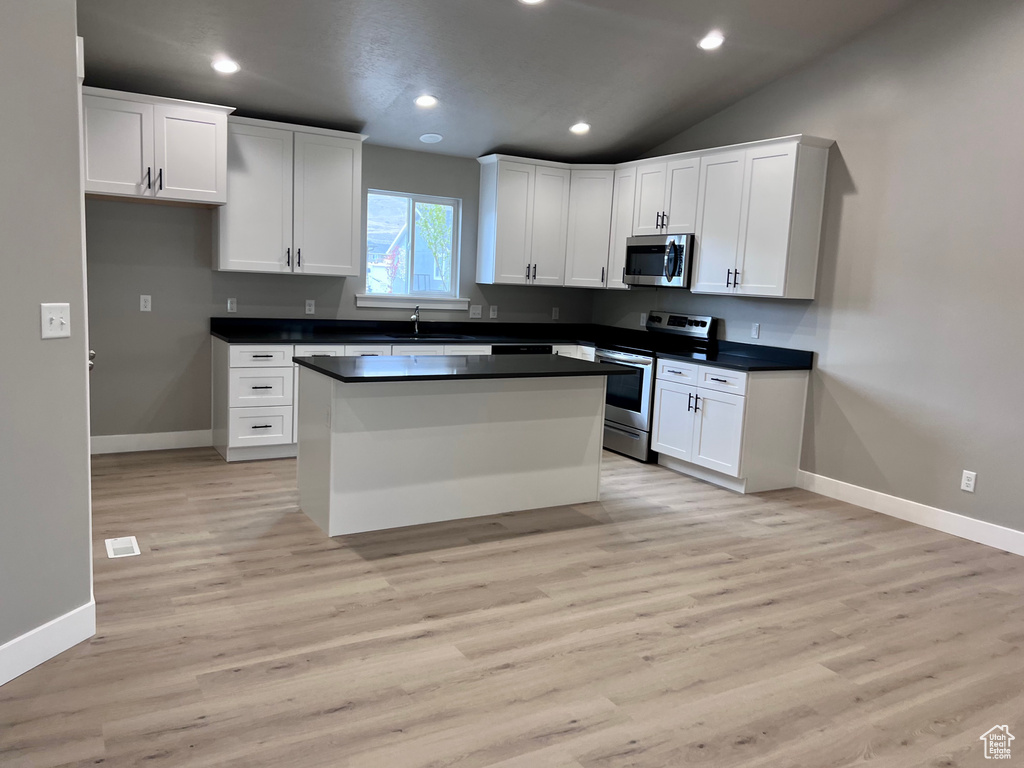 Kitchen with appliances with stainless steel finishes, dark countertops, baseboards, white cabinets, and recessed lighting