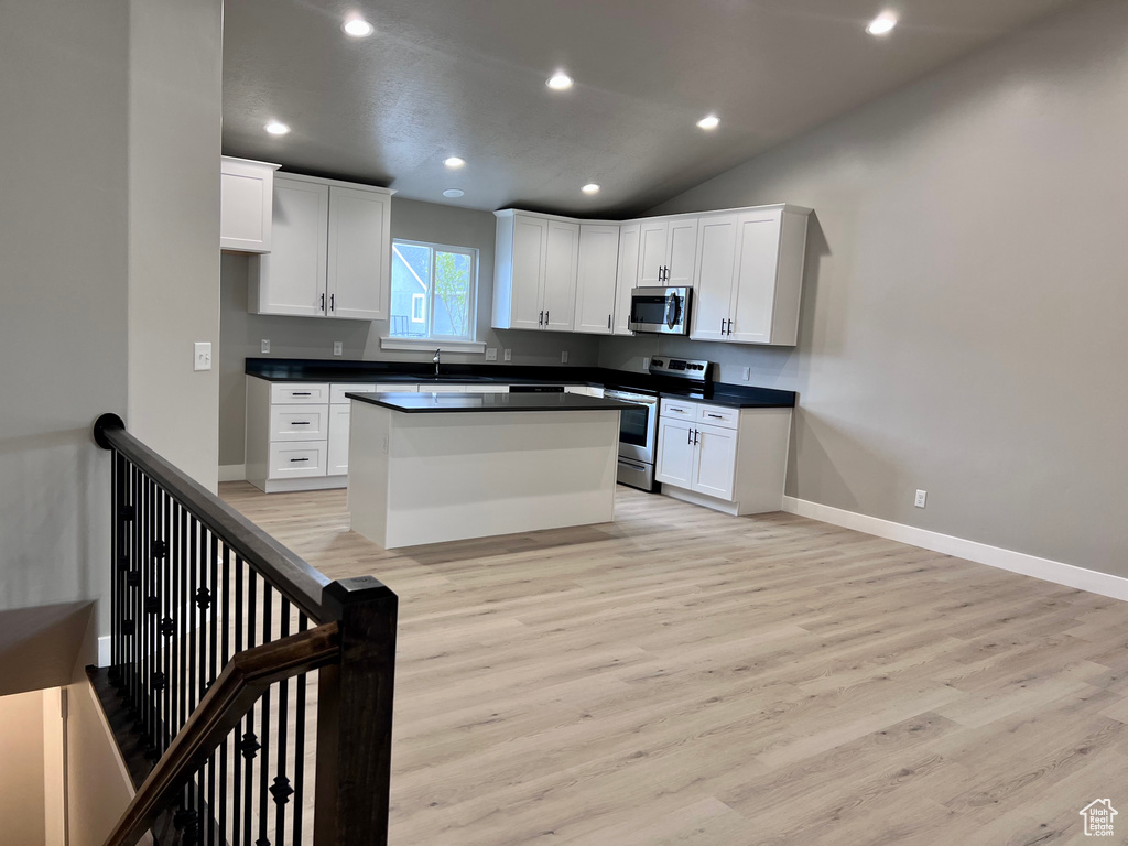 Kitchen featuring stainless steel appliances, dark countertops, light wood-type flooring, white cabinets, and recessed lighting