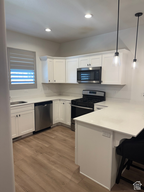 Kitchen with stainless steel appliances, a peninsula, white cabinets, a breakfast bar area, and recessed lighting