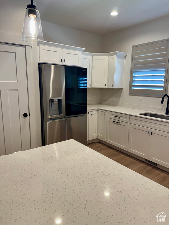 Kitchen with stainless steel refrigerator with ice dispenser, a sink, white cabinetry, dark wood-type flooring, and hanging light fixtures