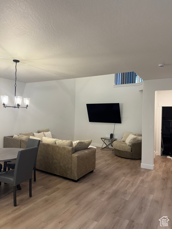 Living room with light wood-type flooring, a chandelier, baseboards, and a textured ceiling