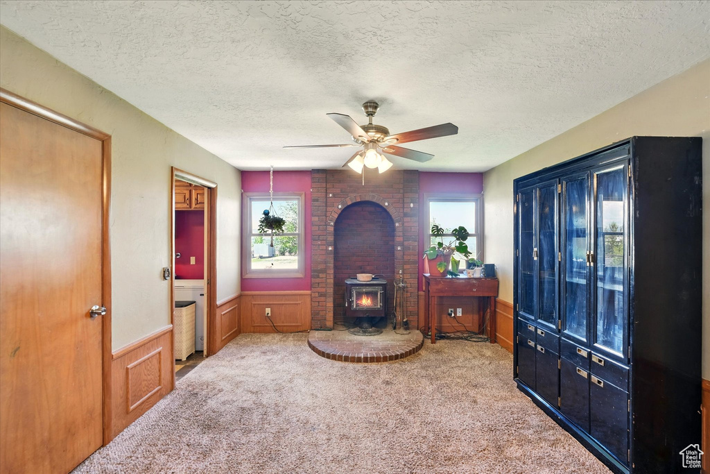 Carpeted living area featuring a wood stove, a wainscoted wall, a ceiling fan, and a textured ceiling