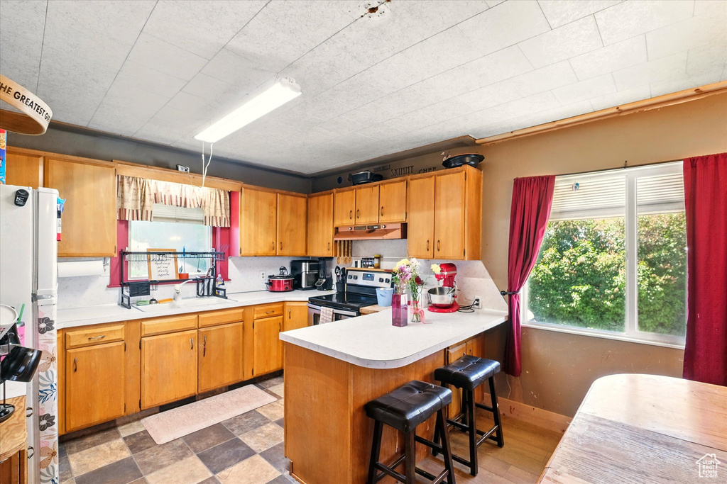 Kitchen featuring stainless steel range with electric cooktop, a sink, under cabinet range hood, light countertops, and a peninsula