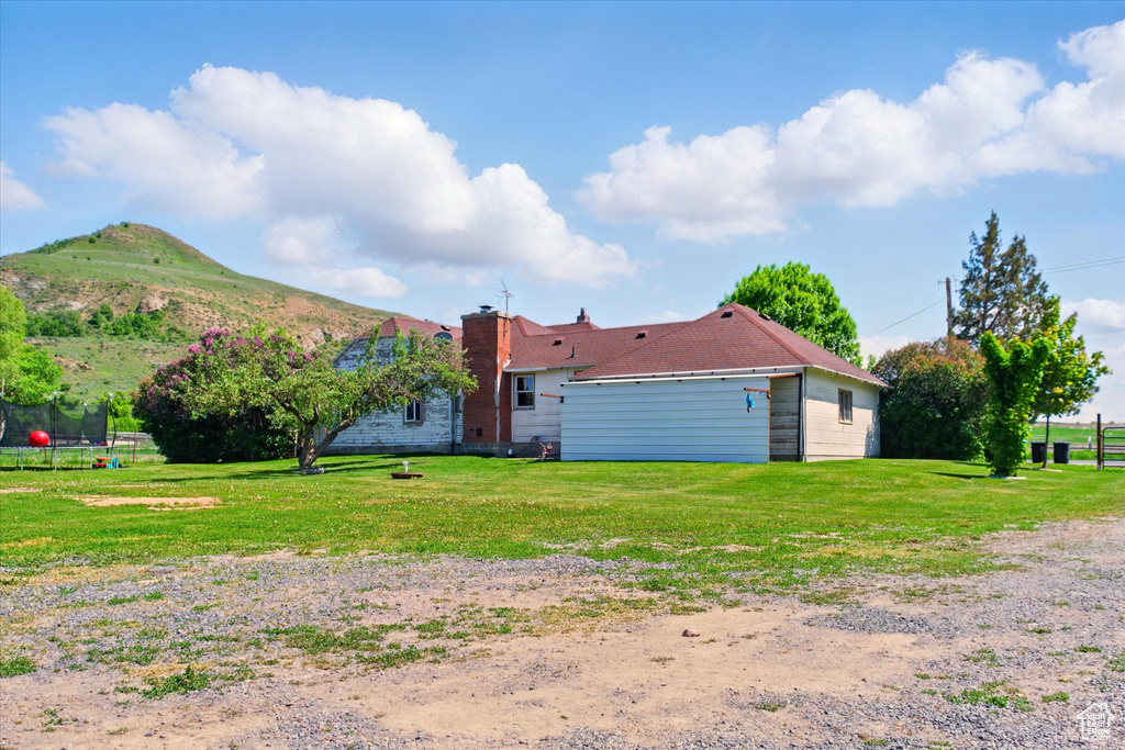 Rear view of house featuring a trampoline, a lawn, a mountain view, and a chimney