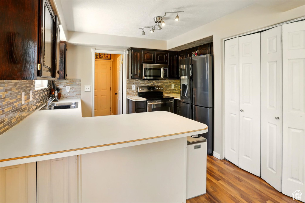 Kitchen with stainless steel appliances, a sink, light countertops, decorative backsplash, and a peninsula