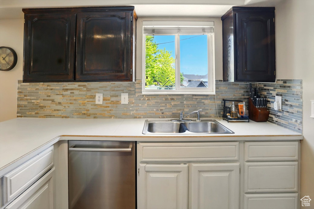 Kitchen with stainless steel dishwasher, a sink, light countertops, and decorative backsplash