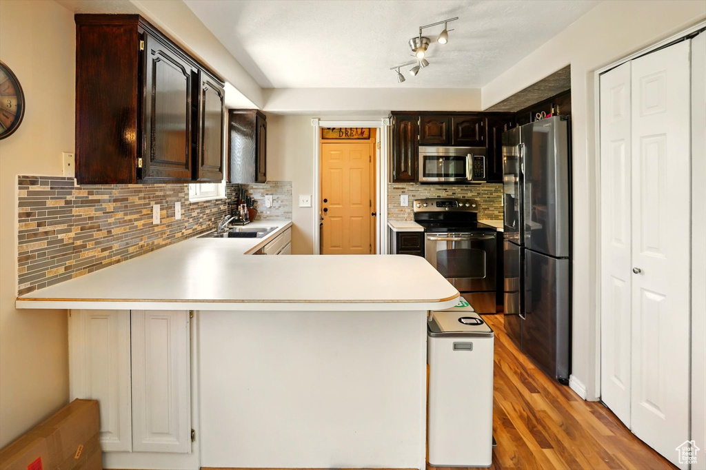 Kitchen with appliances with stainless steel finishes, a peninsula, a sink, light countertops, and backsplash