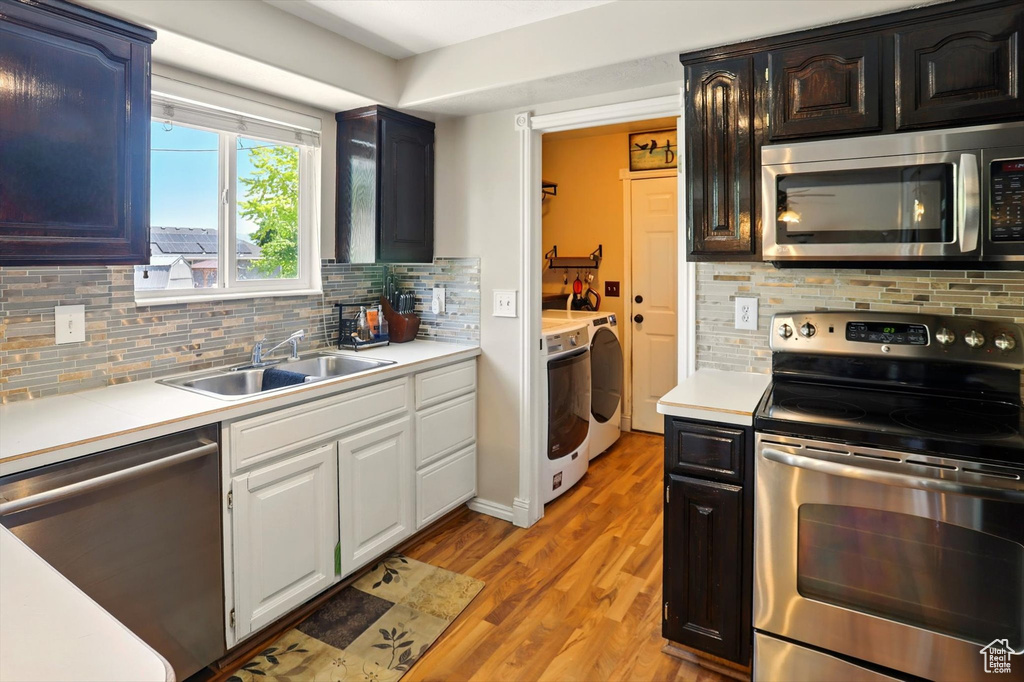 Kitchen with stainless steel appliances, independent washer and dryer, a sink, light wood-style floors, and light countertops