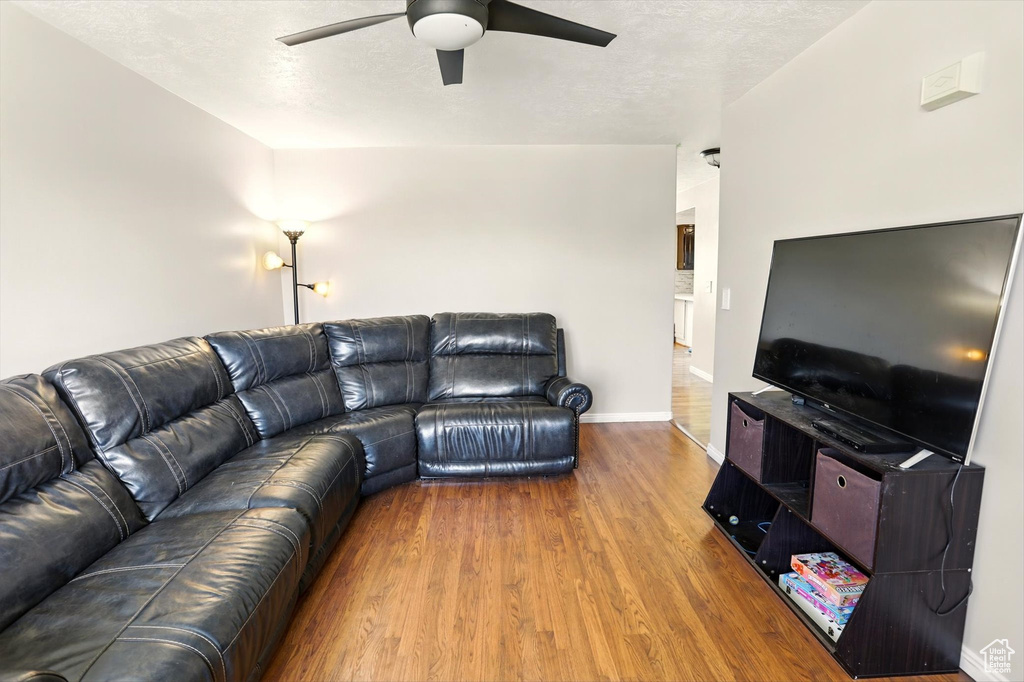 Living room featuring a ceiling fan, wood finished floors, baseboards, and a textured ceiling