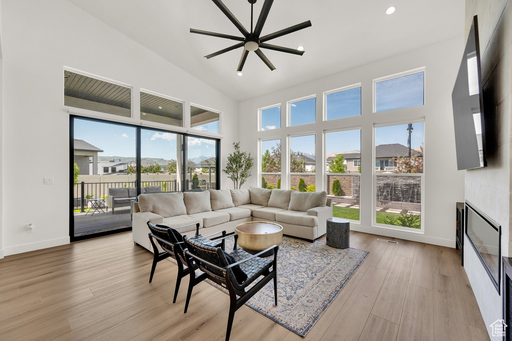 Living area featuring a towering ceiling, a glass covered fireplace, baseboards, and light wood finished floors