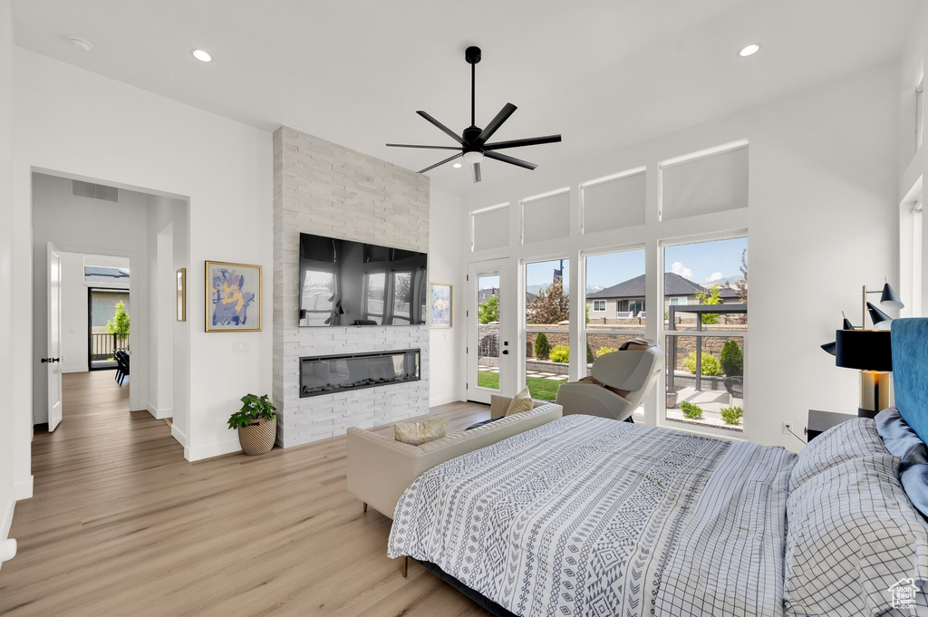Bedroom with wood finished floors, a stone fireplace, a high ceiling, recessed lighting, and baseboards