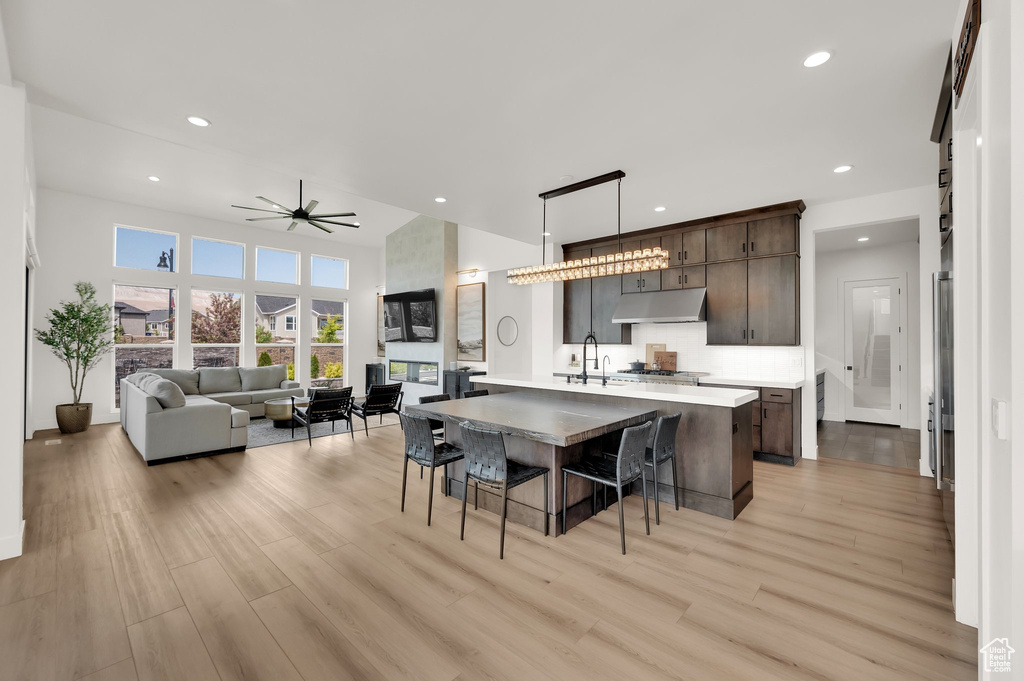 Kitchen with under cabinet range hood, light wood finished floors, dark brown cabinets, light countertops, and recessed lighting