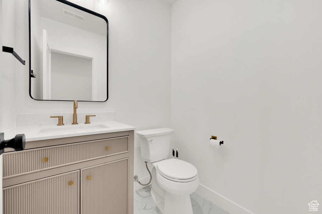 Half bath with toilet, marble finish floors, vanity, and baseboards