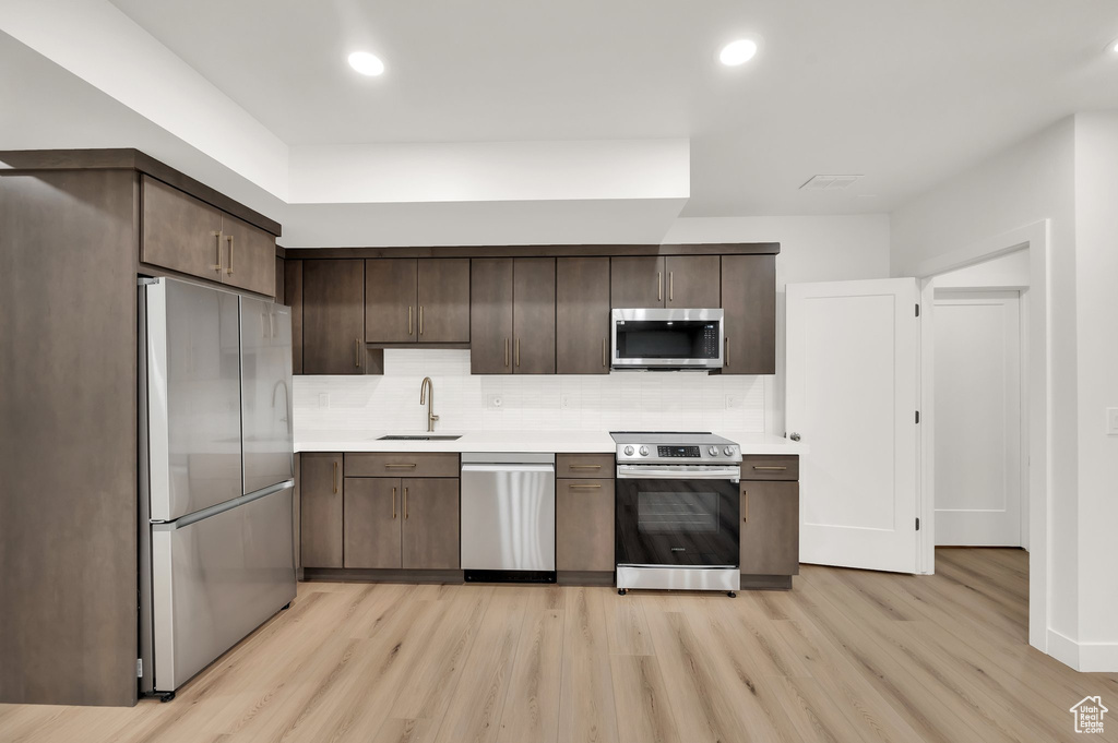Kitchen featuring stainless steel appliances, a sink, light wood finished floors, dark brown cabinetry, and recessed lighting