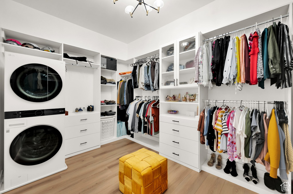 Spacious closet with stacked washer / drying machine, light wood-style floors, and a chandelier