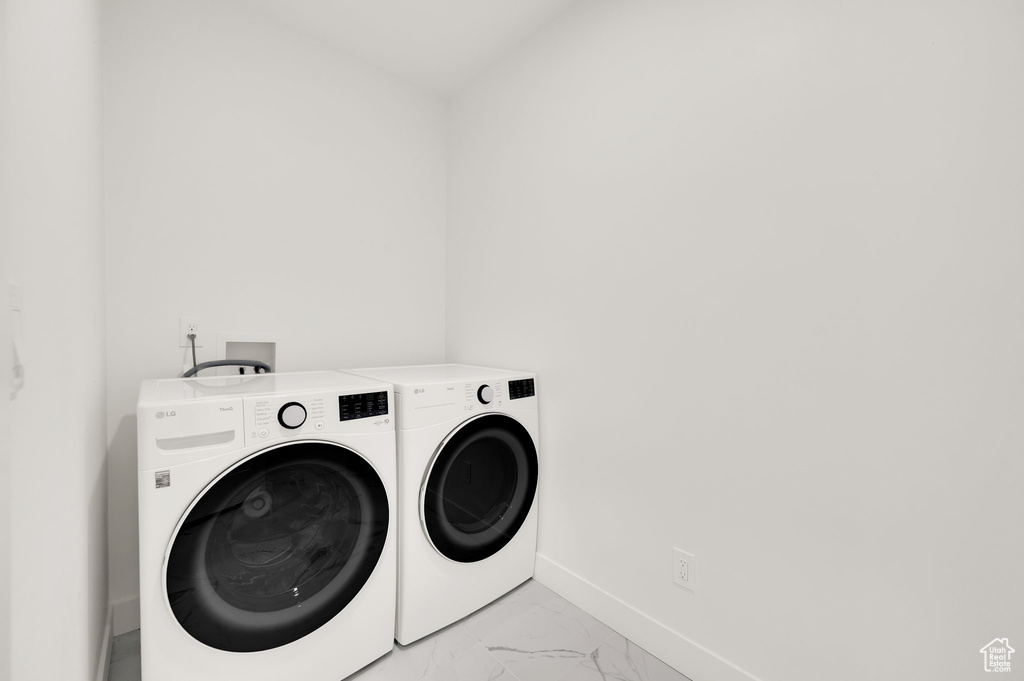 Laundry room featuring separate washer and dryer, light marble finish floors, and baseboards
