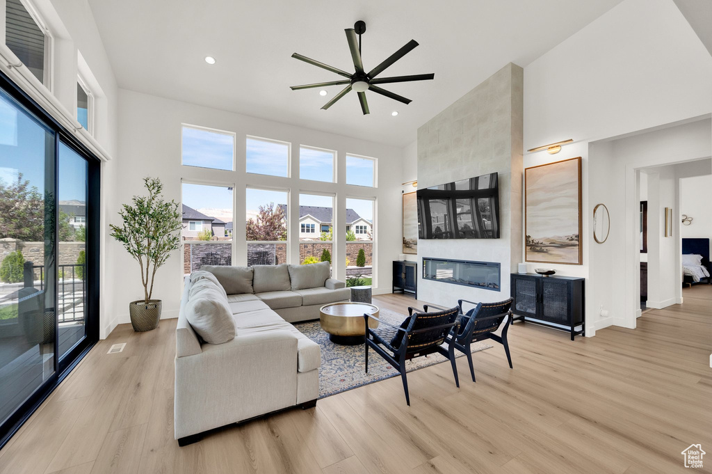 Living room with a high ceiling, a large fireplace, light wood-style floors, recessed lighting, and a ceiling fan