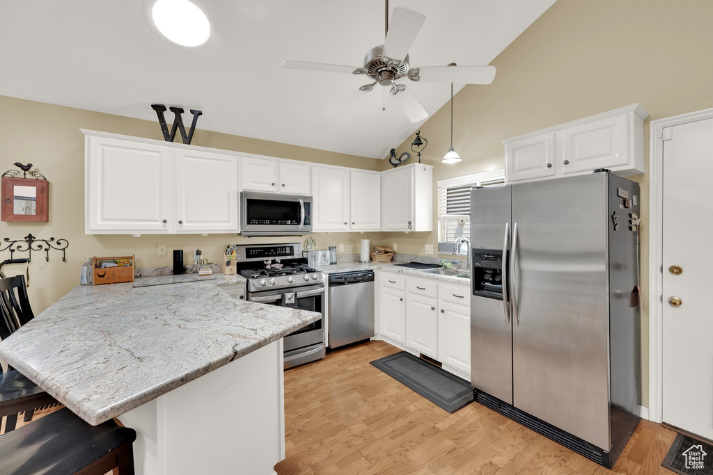 Kitchen with stainless steel appliances, a peninsula, white cabinetry, ceiling fan, and high vaulted ceiling