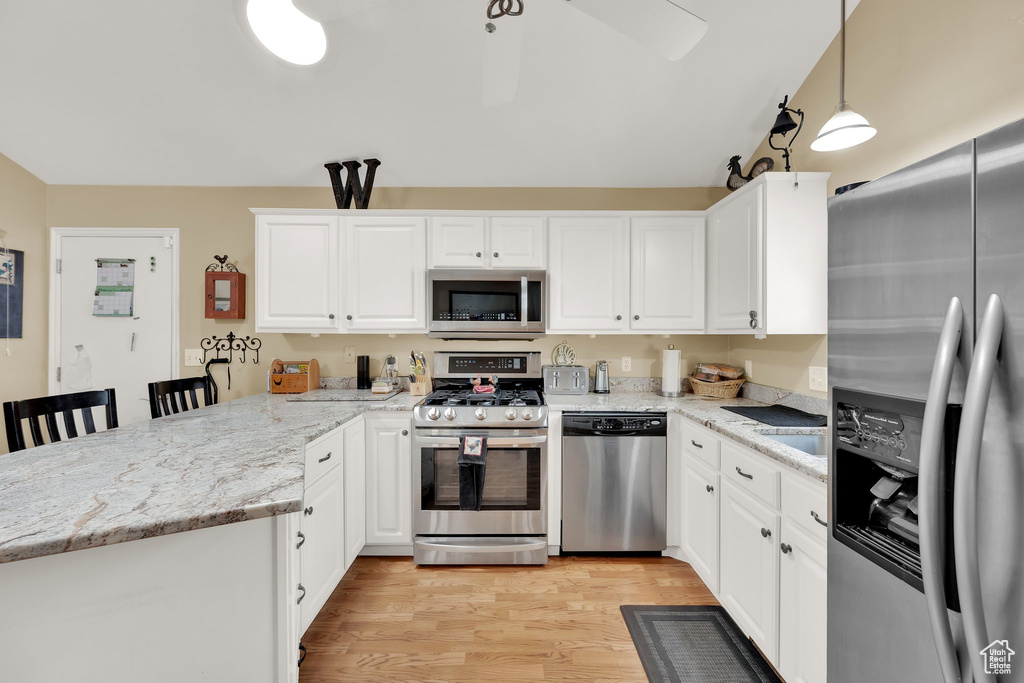 Kitchen with appliances with stainless steel finishes, a peninsula, light wood finished floors, white cabinets, and light stone counters