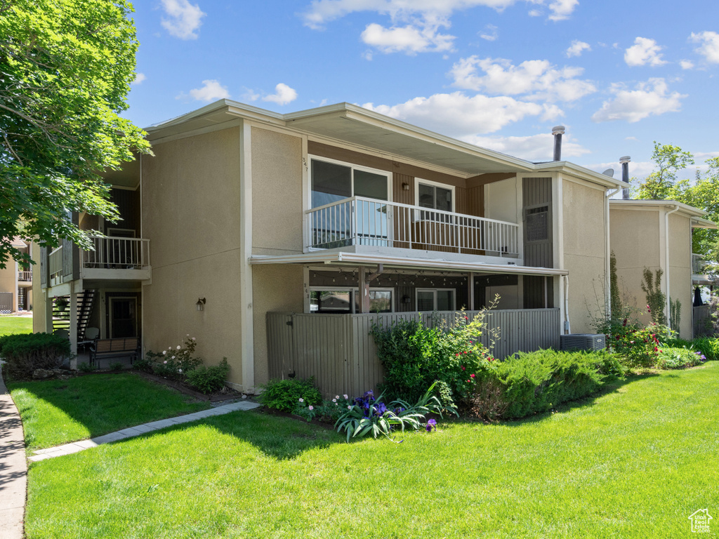 Back of house with a balcony, a yard, and stucco siding