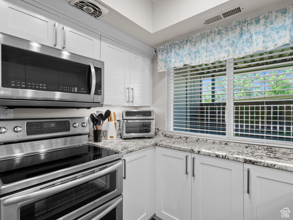 Kitchen featuring stainless steel appliances, white cabinetry, and light stone counters