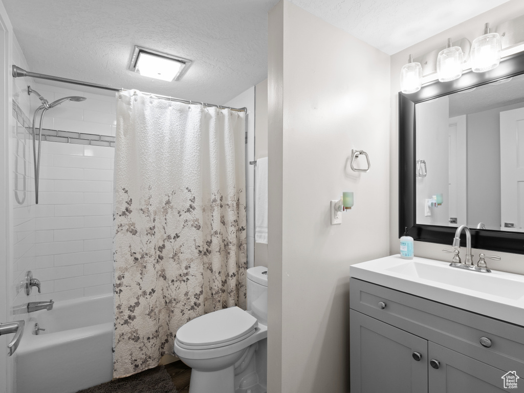 Bathroom featuring toilet, a textured ceiling, vanity, and shower / tub combo with curtain