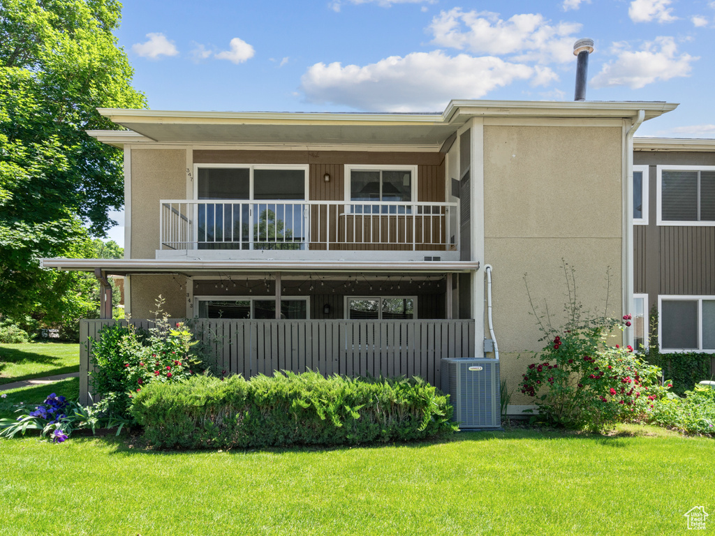 Back of property with a balcony, central AC unit, a yard, and stucco siding