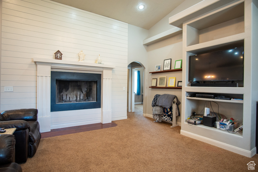 Carpeted living room featuring arched walkways, vaulted ceiling, a fireplace, and recessed lighting