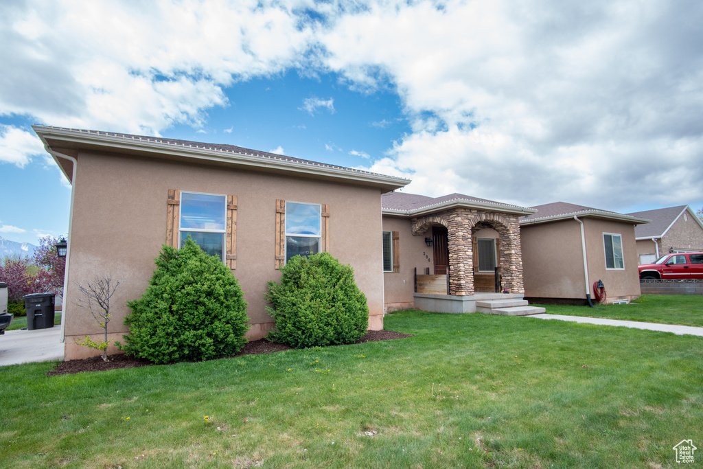 View of front of house featuring stucco siding, a front lawn, and stone siding