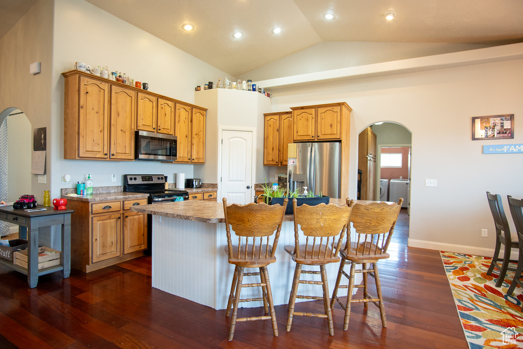 Kitchen with stainless steel appliances, arched walkways, washing machine and clothes dryer, a center island with sink, and dark wood-style floors