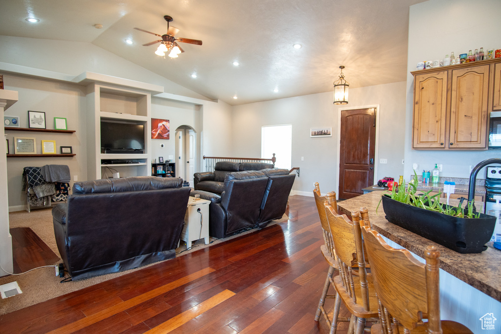 Living room featuring a ceiling fan, arched walkways, dark wood-type flooring, vaulted ceiling, and recessed lighting