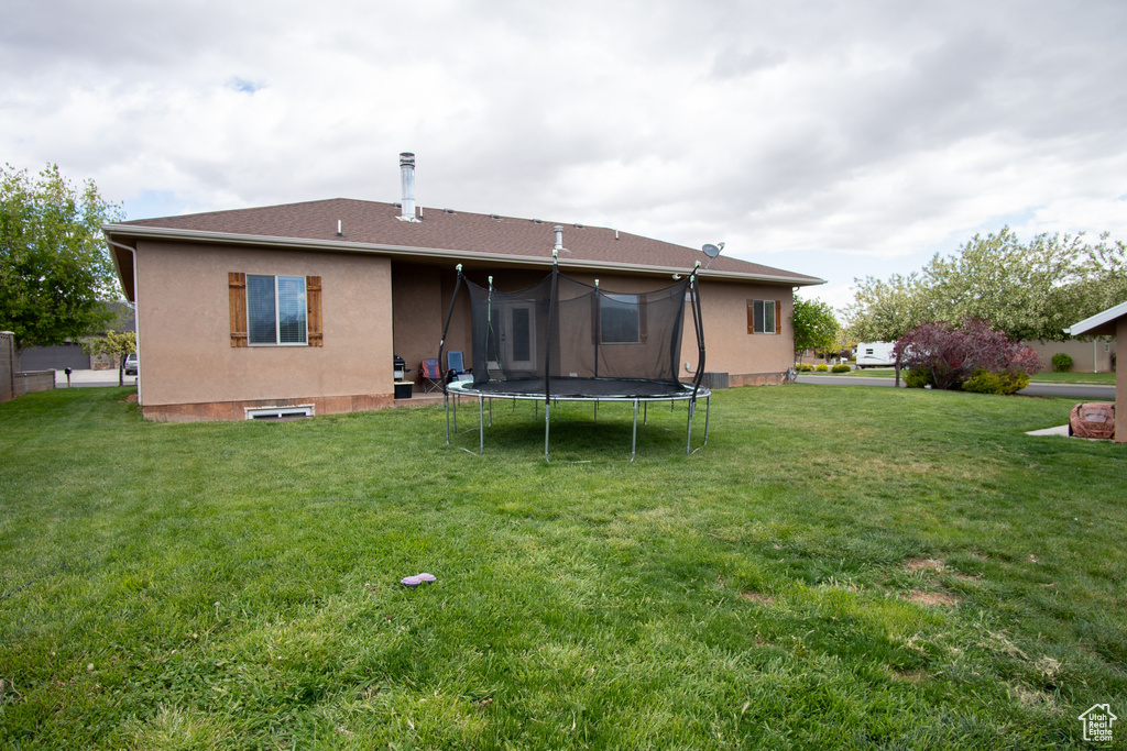 Back of house with a trampoline, a lawn, and stucco siding
