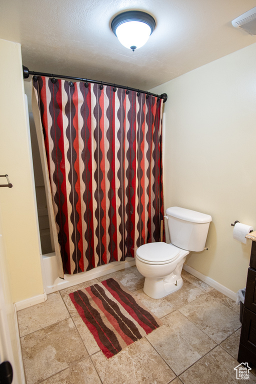 Bathroom with toilet, a shower with shower curtain, and baseboards