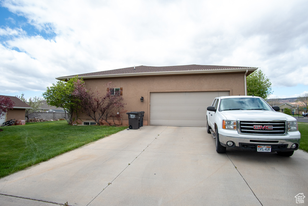 View of side of home with concrete driveway, stucco siding, an attached garage, and a lawn