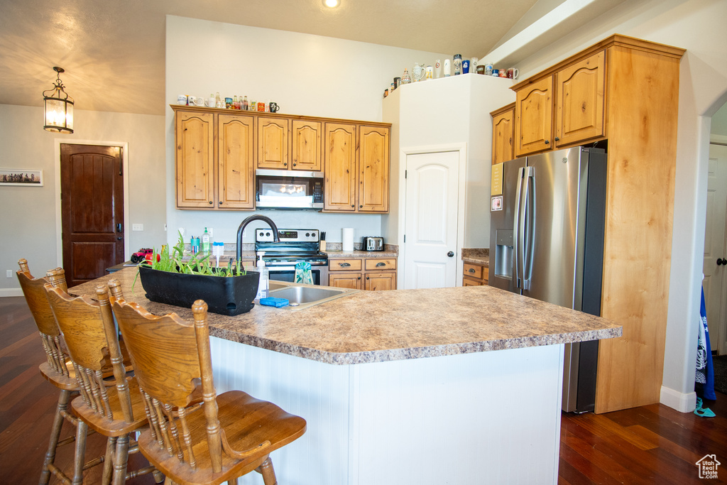 Kitchen with stainless steel appliances, dark wood-type flooring, light countertops, a sink, and a kitchen bar
