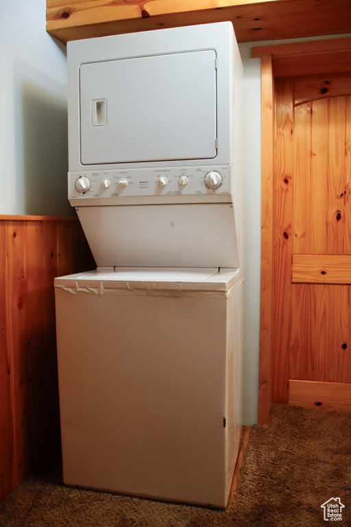 Laundry room with stacked washer and clothes dryer, a wainscoted wall, and carpet flooring