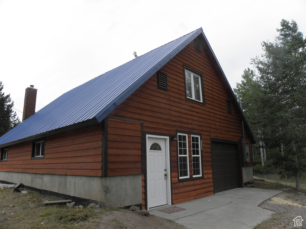 View of home's exterior featuring a garage, metal roof, a chimney, and driveway